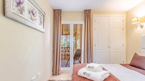 A hotel room with a bed, a chair, a door, and a view of the outside. - GuestReady - Santa Maria Village (Marbella)
