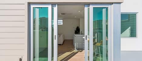 Un bâtiment moderne doté d’une entrée avec une porte vitrée coulissante, d’un intérieur visible avec un canapé et un meuble, et offrant une vue dégagée sur l’extérieur.