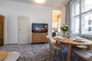 Ein Essbereich mit einem runden Tisch, Stühlen, einem Fernseher und einer Küche im Hintergrund.