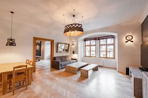 Ein modernes Wohnzimmer mit Holzboden im Fischgrätmuster, einem Esstisch mit Stühlen, einem Sofa, einem Couchtisch und einem großen Fenster mit Aussicht.