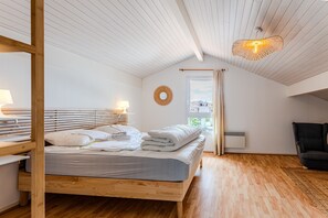 Makuuhuoneessa on puinen sänky, yöpöydät, riippuvalaisin ja ikkuna, jossa on verhot.