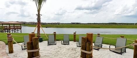 A beach area with lounge chairs and a palm tree, overlooking a body of water.