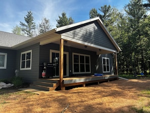 A single-story house with a covered porch, a grill, and a blue container.