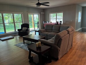 A spacious living room with a large window, a ceiling fan, a sofa, a coffee table, and a dining table with chairs. - Beautiful lakefront house on Petenwell Lake
 162 feet of lake frontage and dock. (Necedah)