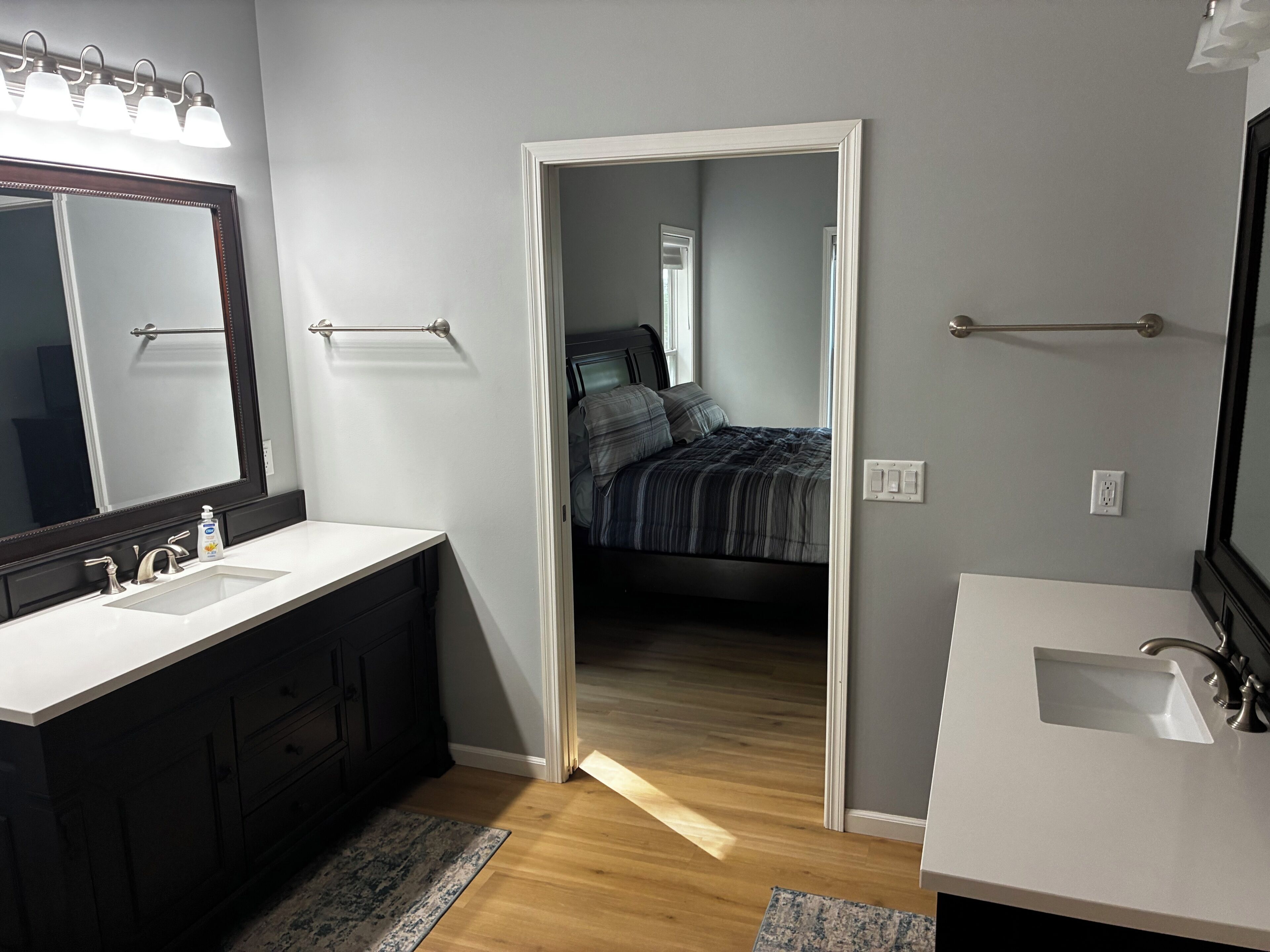 A bathroom with two sinks, a mirror, and a door leading to a bedroom.