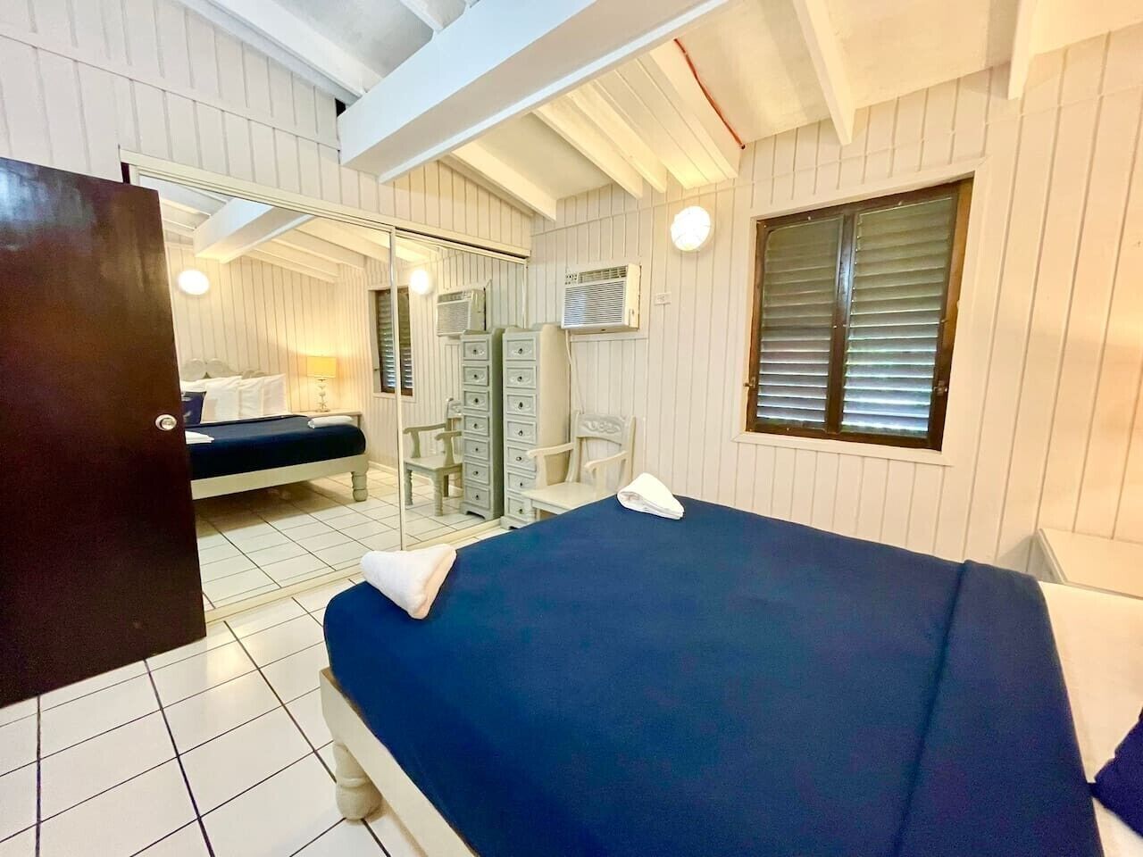 Une chambre à coucher avec un lit, une commode, une chaise et une fenêtre avec des stores.