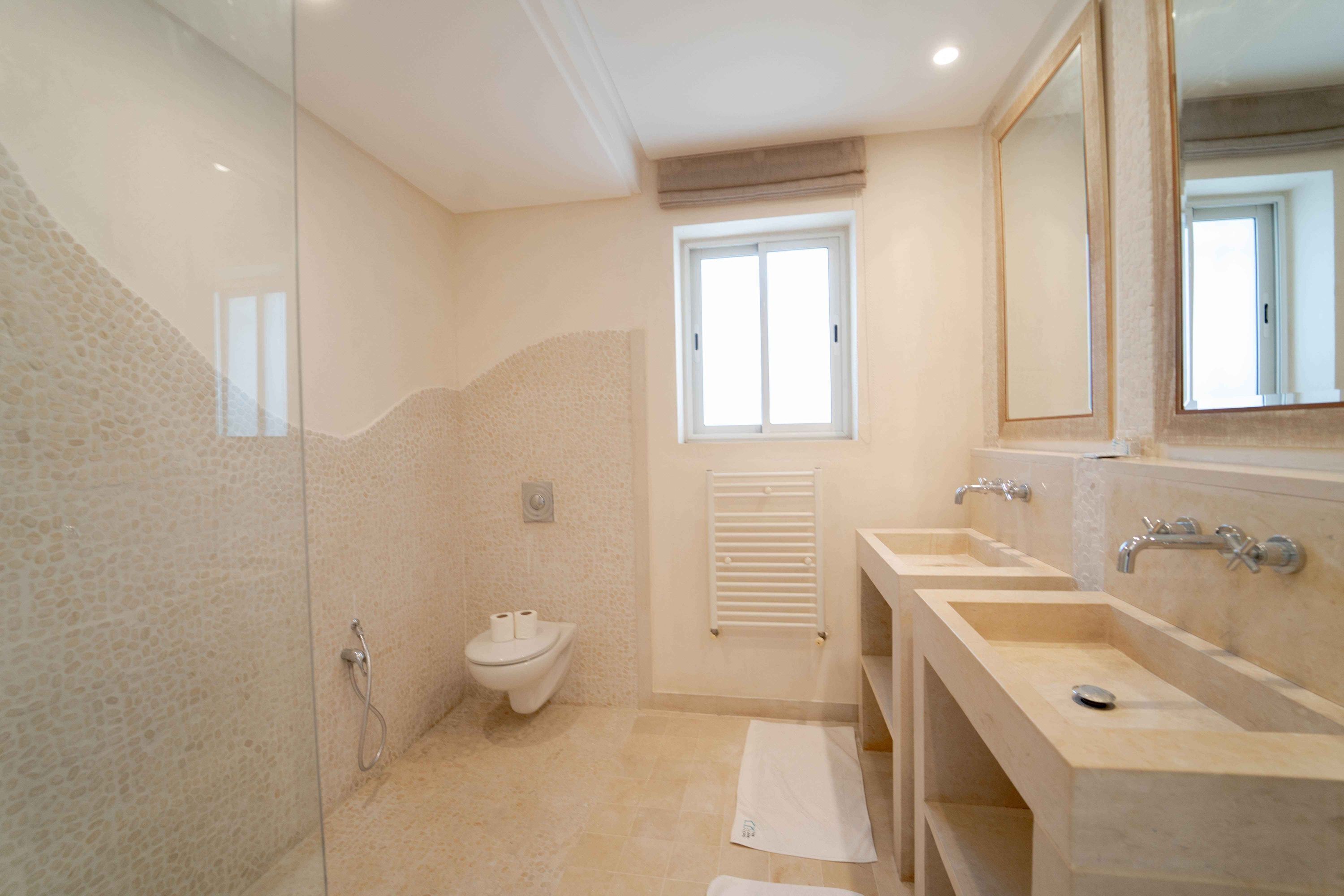Une salle de bain dotée d’une douche à parois de verre, de toilettes, d’un bidet et d’un meuble-lavabo avec deux vasques.
