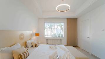 A hotel room with a large bed, a window with a view, a ceiling light fixture, and a door.