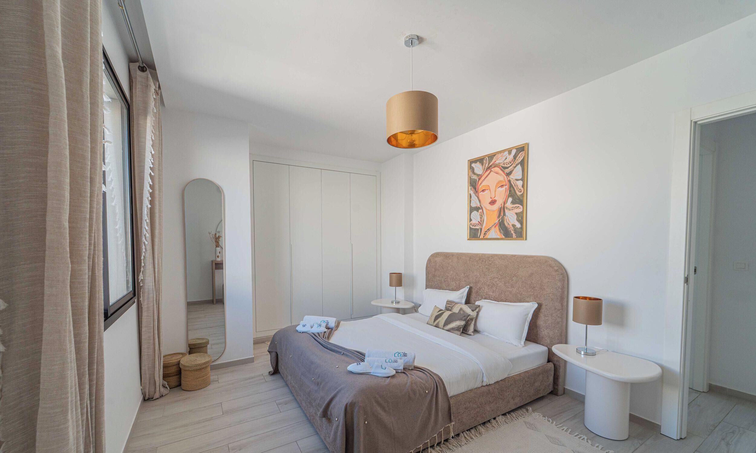 Une chambre à coucher comprenant un lit, des tables de chevet, un luminaire suspendu, un tableau et une armoire.