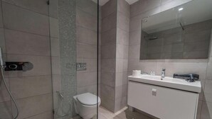 A modern bathroom with a glass shower enclosure, a toilet, and a white vanity with a mirror. - New 2BR Apt Parking Netflix La Marsa (La Marsa)