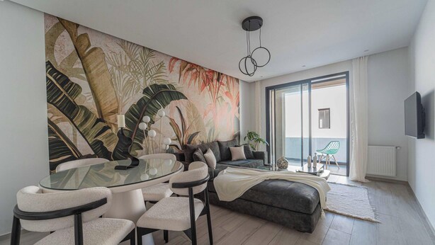 A modern living room with a glass dining table, a sofa, and a large tropical mural on the wall. - New 2BR Apt Parking Netflix La Marsa (La Marsa)
