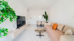 A modern living room with a flat-screen TV, a sofa, a coffee table, and a dining area. - New 2BR Sunny Balcony Jardins Carthage (Tunis)