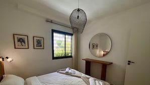 A hotel room with a bed, a bedside table, a hanging light fixture, a window, and a mirror. - Chic Boho 1BR Modern Comfort (La Marsa)