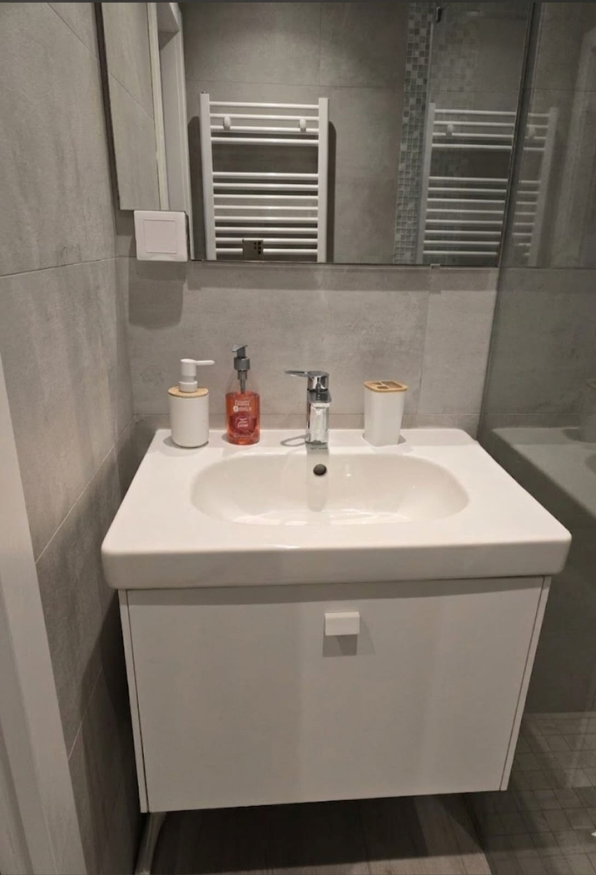 Une salle de bain avec un lavabo blanc, un miroir, un porte-serviettes et un distributeur de savon.