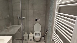 A modern bathroom with a glass shower enclosure, a white toilet, and a built-in towel rack. - Chic Boho 1BR Modern Comfort (La Marsa)