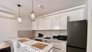 A modern kitchen with white cabinetry, a black refrigerator, a microwave, and a coffee maker. There are two white chairs and a small table. - Chic Boho 1BR Modern Comfort (La Marsa)
