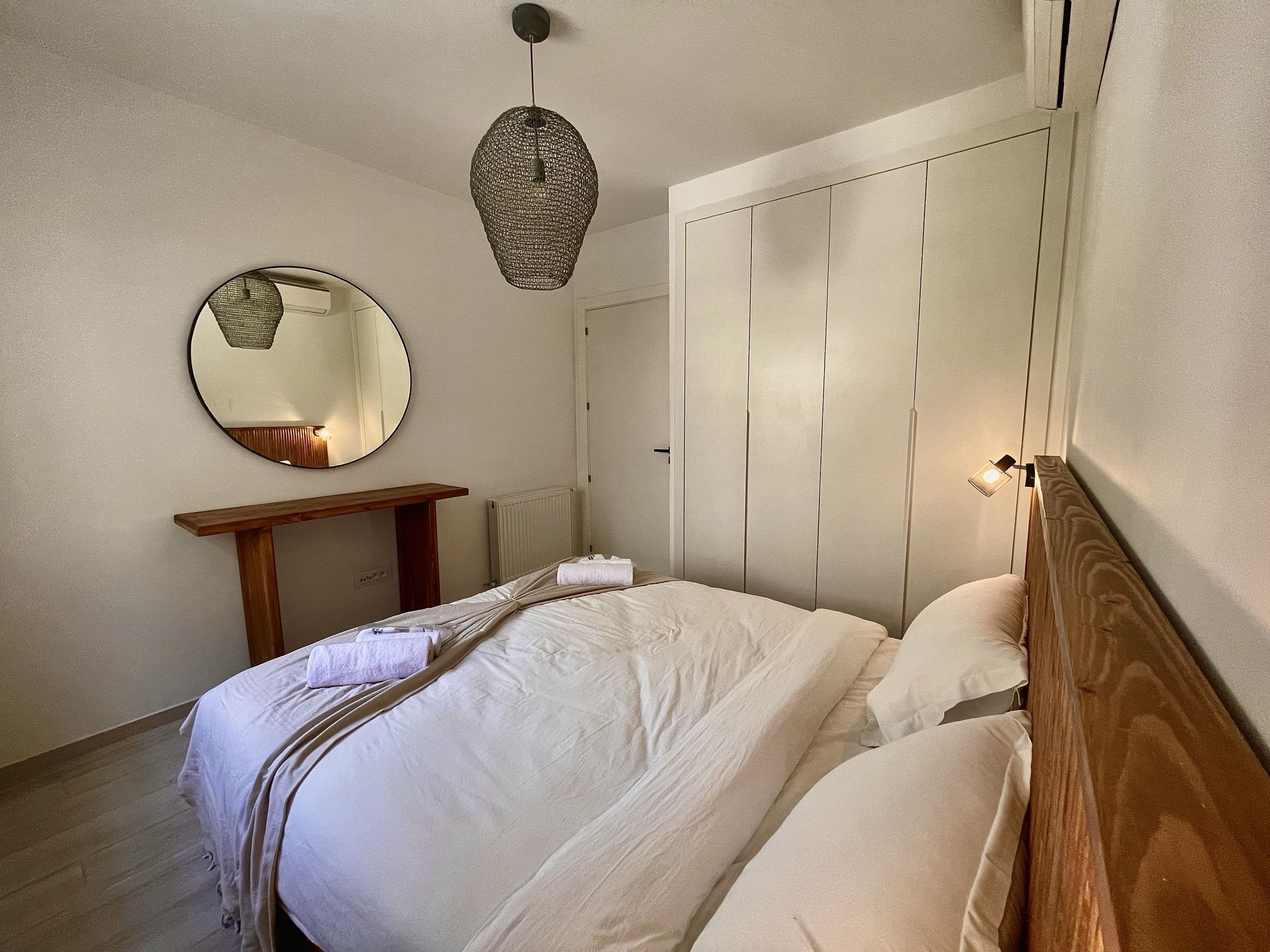 Une chambre à coucher comprenant un lit, une table de chevet, un miroir, une armoire et un luminaire suspendu.