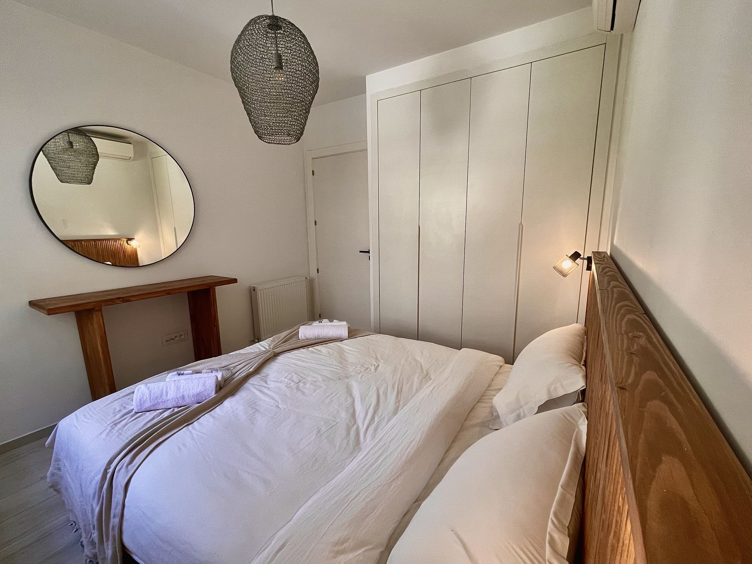 A bedroom with a bed, a bedside table, a mirror, a hanging light fixture, and a wardrobe.