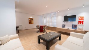 Ein modernes Wohnzimmer mit einer Couch, einem Couchtisch, einem roten Tisch mit Stühlen, einem an der Wand montierten Fernseher und Kunstwerken an den Wänden.