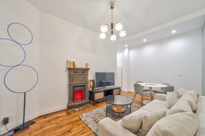 Ein modernes Wohnzimmer mit Kamin, Fernseher, einer Couch und einem Essbereich.