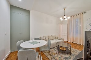 A modern living room with a round dining table, a sofa, a glass coffee table, and a TV. - Renovated 1BD Walk to 6th 7th and Montparnass (Paris)