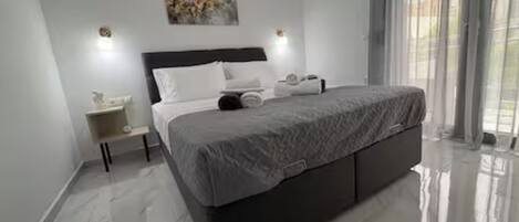 A modern bedroom with a large bed, a nightstand, an air conditioning unit, and a window with curtains.