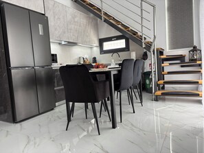 A modern kitchen with a stainless steel refrigerator, a built-in oven, and a microwave. There is a dining table with chairs, and a staircase with wooden steps leading to an upper level. - Villa Elena- Peris, By IdealStay Experience (Gouves)