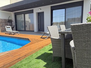 A modern outdoor area with a swimming pool, wicker furniture, and a stone wall. - Villa Elena- Peris, By IdealStay Experience (Gouves)
