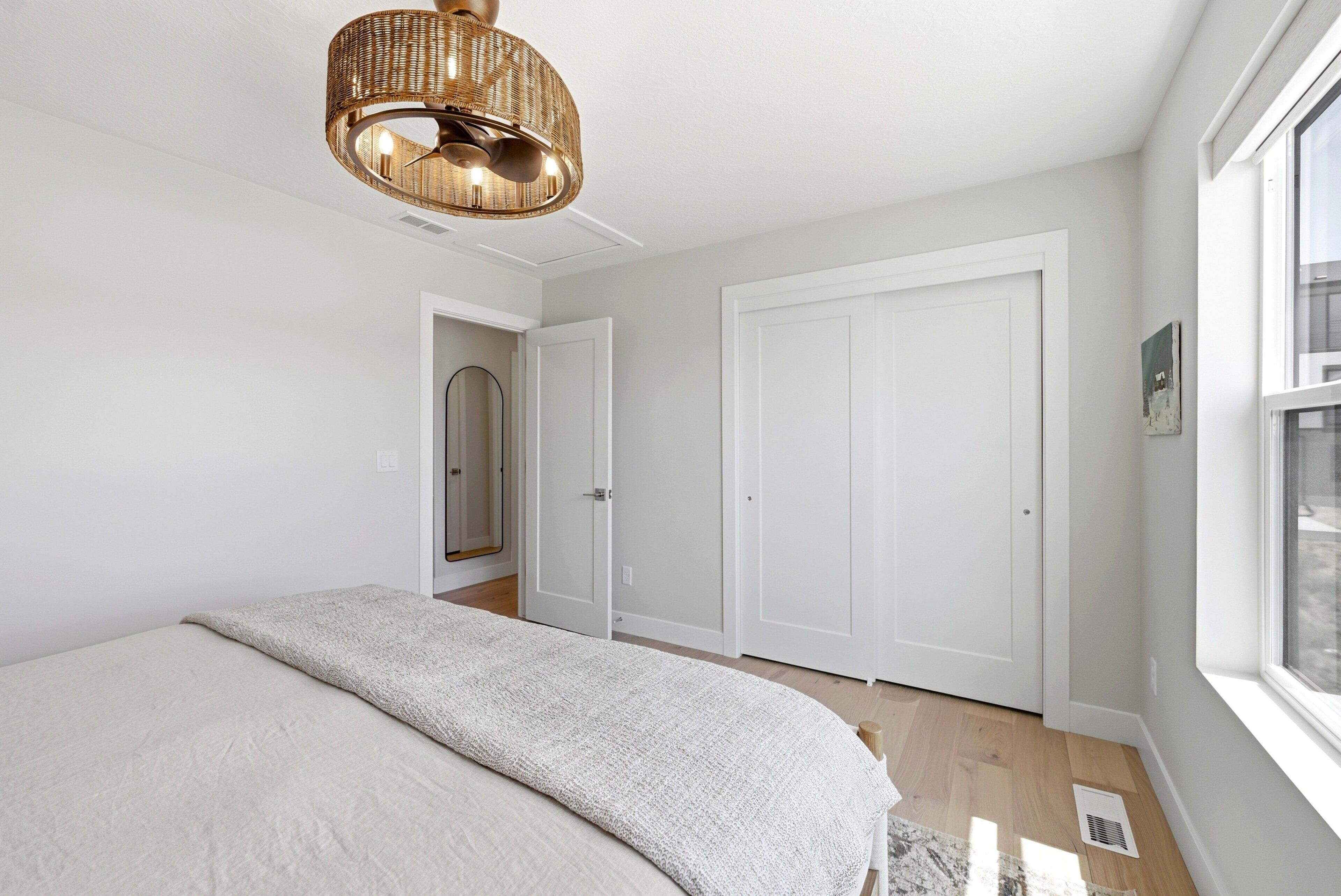 A bedroom with a bed, a wicker ceiling light, white doors, and a window.
