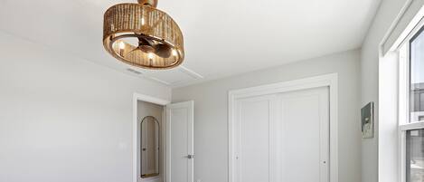 A bedroom with a bed, a wicker ceiling light, white doors, and a window.