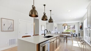 Una cocina moderna con una isla central, iluminación colgante y vista al área de estar.