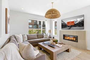 Ein modernes Wohnzimmer mit Sofa, Couchtisch, Kamin und einem großen Fernseher.