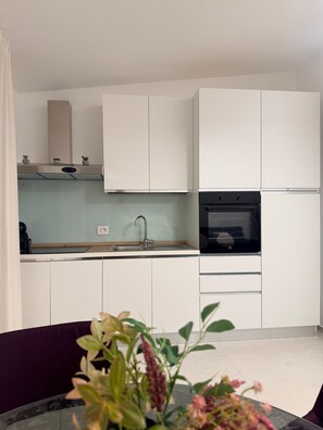 A modern kitchen with white cabinets, a stainless steel sink, and a built-in oven.