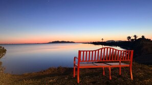 A bench by a calm body of water with a sunset in the background.