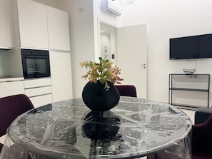 A modern kitchen with white cabinets, a black oven, and a dining area with a glass table covered in plastic.