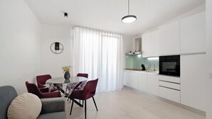 Cocina moderna con armarios blancos, horno negro y zona de comedor con mesa redonda y sillas rojas.