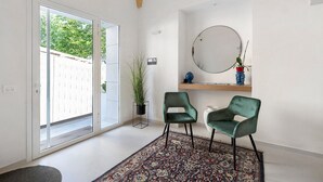 A modern room with a sliding glass door, a patterned rug, two green chairs, a round mirror, and a potted plant. - Apartment 'Palazzo Tilde - 1 B' with Sea View, Wi-Fi and Air Conditioning (Marsala)