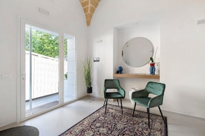 Ein Zimmer mit einer Schiebetür, einem Blumentopf, zwei Stühlen, einem runden Spiegel und einem Regal mit Dekoration.