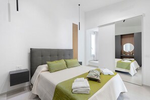 Een moderne slaapkamer met een groot bed, een nachtkastje, een spiegel en uitzicht op een badkamer.