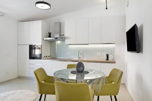 Een moderne keuken met witte kastjes, een inbouwoven en een eethoek met een ronde tafel en gele stoelen.