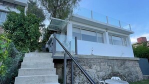 Un bâtiment moderne avec un escalier menant à un balcon en verre, le tout entouré de verdure.