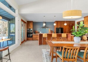 A modern kitchen with wooden cabinets, a dining area with a large table and chairs, and a hanging light fixture.