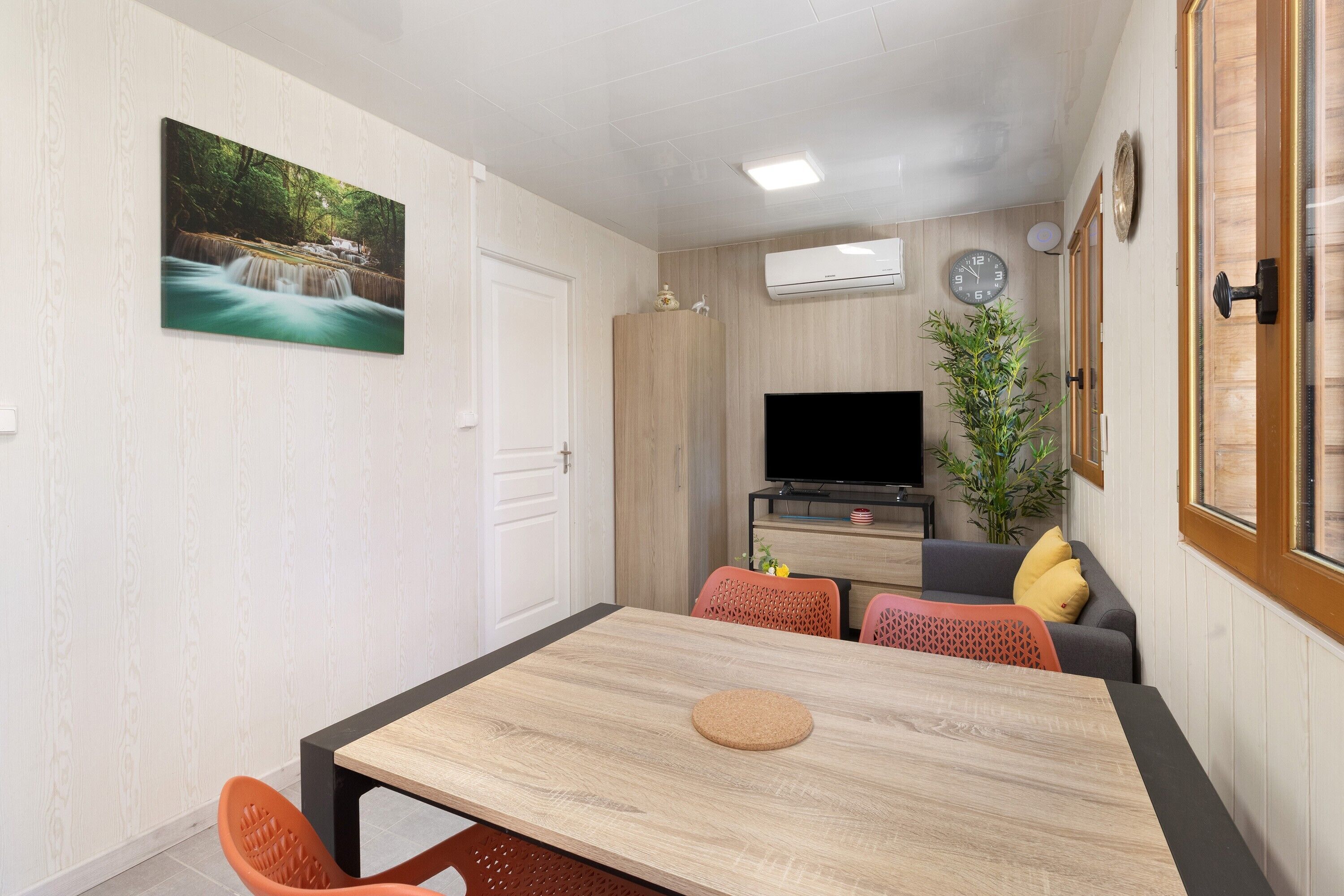 A room with a wooden dining table, a TV, a cabinet, and a plant.