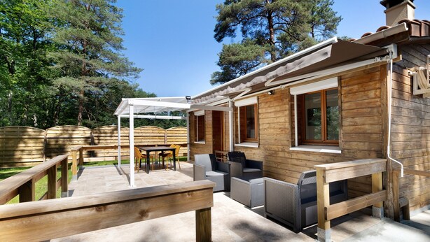 Een houten blokhut met een terras, zitplaatsen buiten en een pergola.