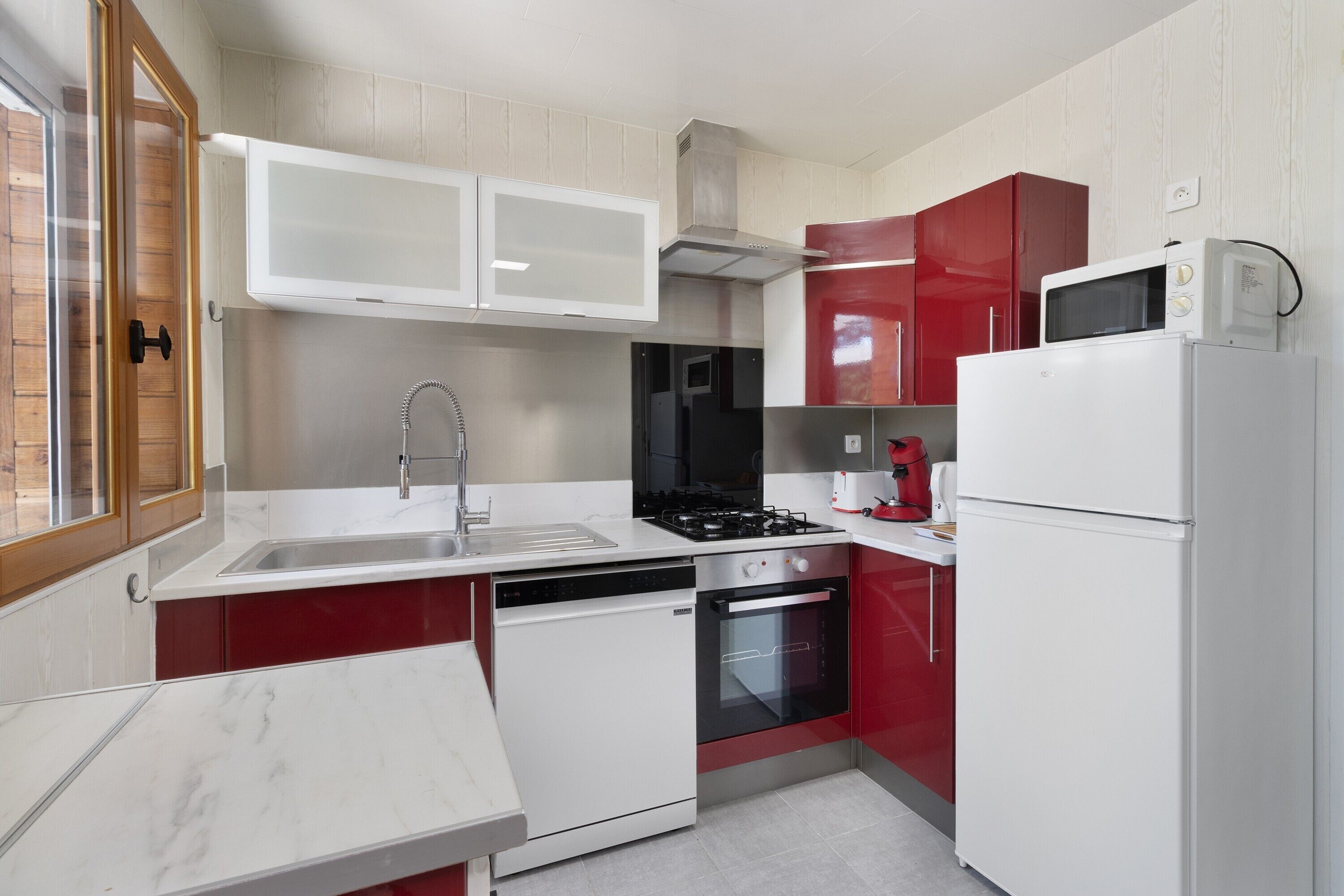 Une cuisine avec des meubles blancs et rouges, un évier en acier inoxydable, une cuisinière, un four et un four à micro-ondes.