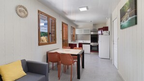 Een ruimtelijke zithoek met eethoek, kitchenette en een bank met kussen.