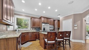 Cocina con armarios de madera, encimeras de granito, microondas integrado y una zona de bar con dos sillas.