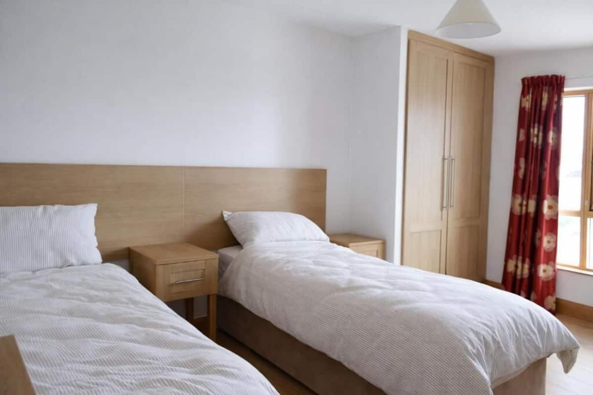 Ein Schlafzimmer mit zwei Betten, Holz-Kopfteilen, einem Kleiderschrank und einem Fenster mit Vorhängen.