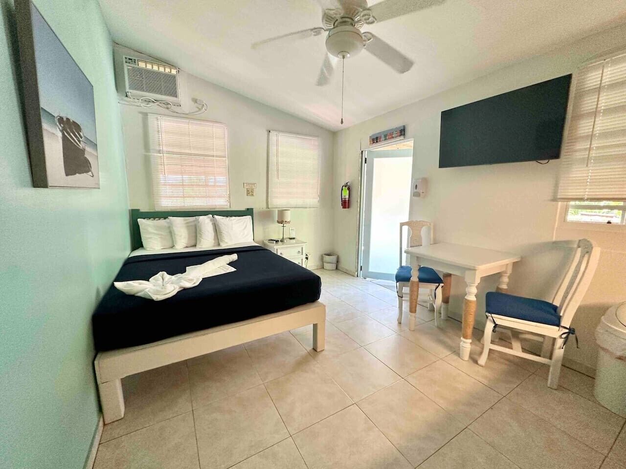 A bedroom with a bed, a desk, a chair, a ceiling fan, and a TV.