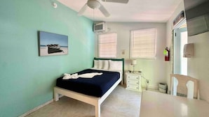 Un dormitorio con cama, ventilador de techo, aire acondicionado, mesita de noche, silla y ventana con persianas.